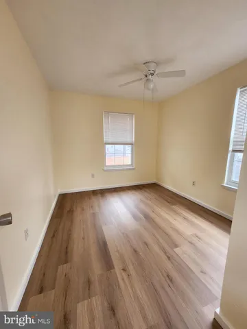an empty room with wooden floor ceiling fan and windows