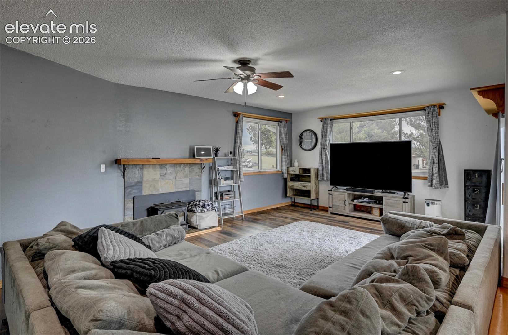 8170 Valli Farm Road Fountain, CO 80817 - Photo 7 of 50 Living area featuring wood-finish flooring, a ceiling fan, and a stone-surround fireplace with a wood mantle