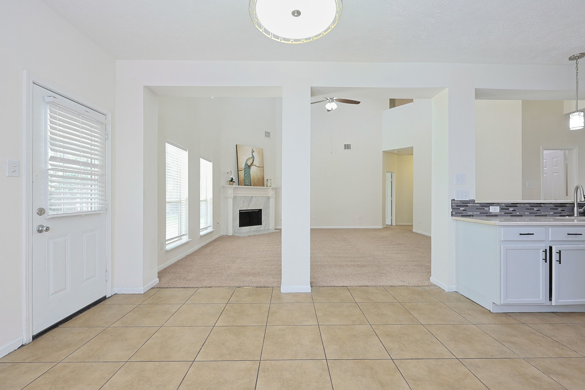 23019 Eastgate Village Drive Spring, TX 77373 - Photo 13 of 46 This bright, open-concept living space features a tiled floor, a cozy carpeted area with a fireplace, large windows for natural light, and a modern kitchen with stylish backsplash and pendant lighting.