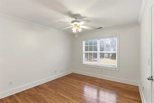 an empty room with wooden floor ceiling fan and windows