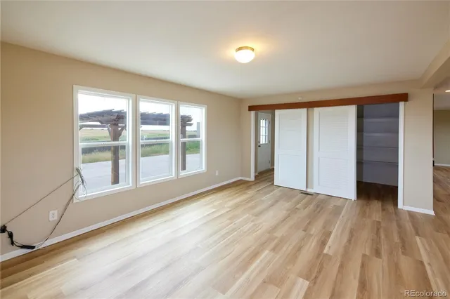 a view of an empty room with a window and wooden floor