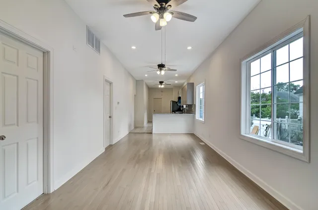 a view of a livingroom with a ceiling fan window hardwood floor and leading from a corridor