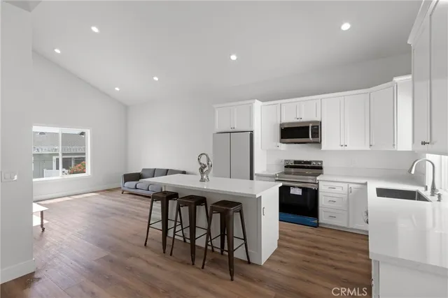 a kitchen with stainless steel appliances granite countertop a stove a sink a microwave a refrigerator with white cabinets and wooden floor