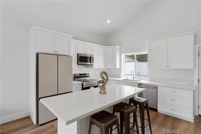 a kitchen with a refrigerator a stove a sink and white cabinets with wooden floor