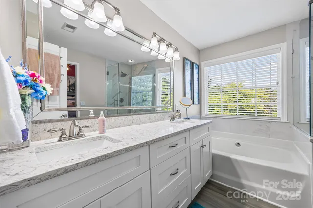 a bathroom with double vanity sinks a large mirror and a bathtub next to a window
