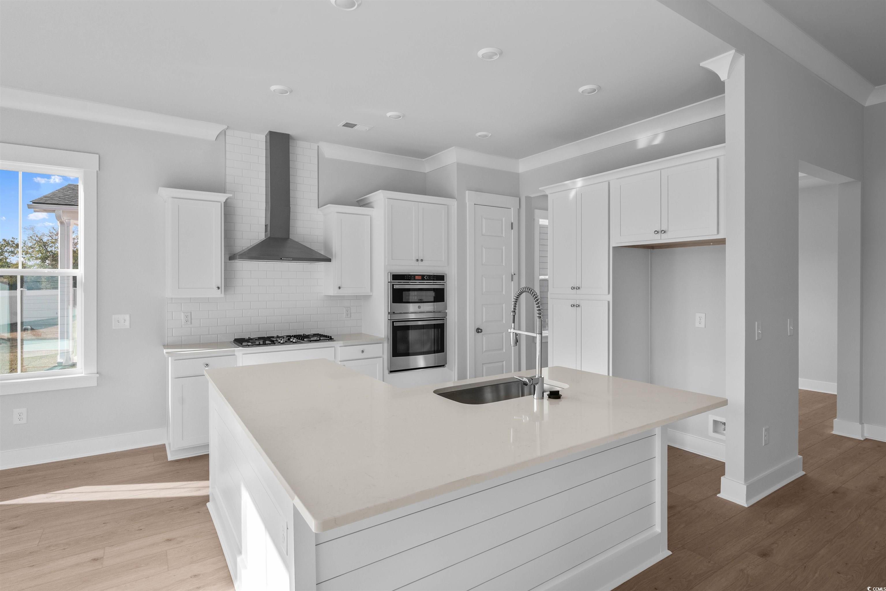 231 Atlantic Breeze Street Myrtle Beach, SC 29572 - Photo 15 of 21 Kitchen featuring white cabinets, a kitchen island with sink, ornamental molding, wall chimney exhaust hood, and tasteful backsplash