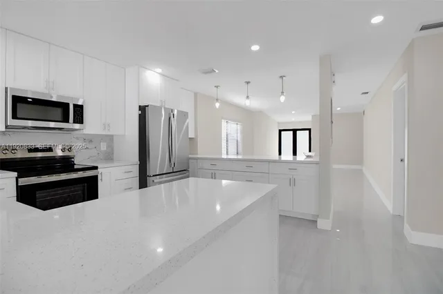 a large kitchen with stainless steel appliances a large counter top a stove a sink a refrigerator and a cabinets