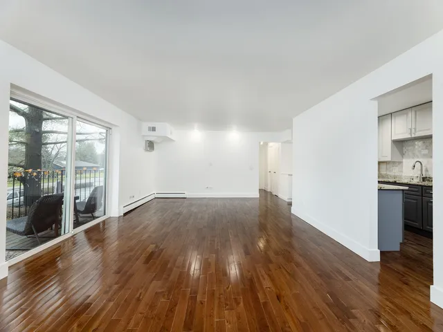 a view of empty room with wooden floor and a kitchen