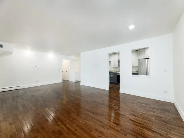 a view of empty room with wooden floor and kitchen