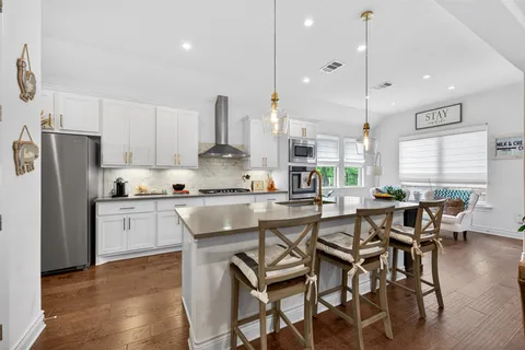 a kitchen with stainless steel appliances granite countertop a table chairs wooden floors a large window and white cabinets