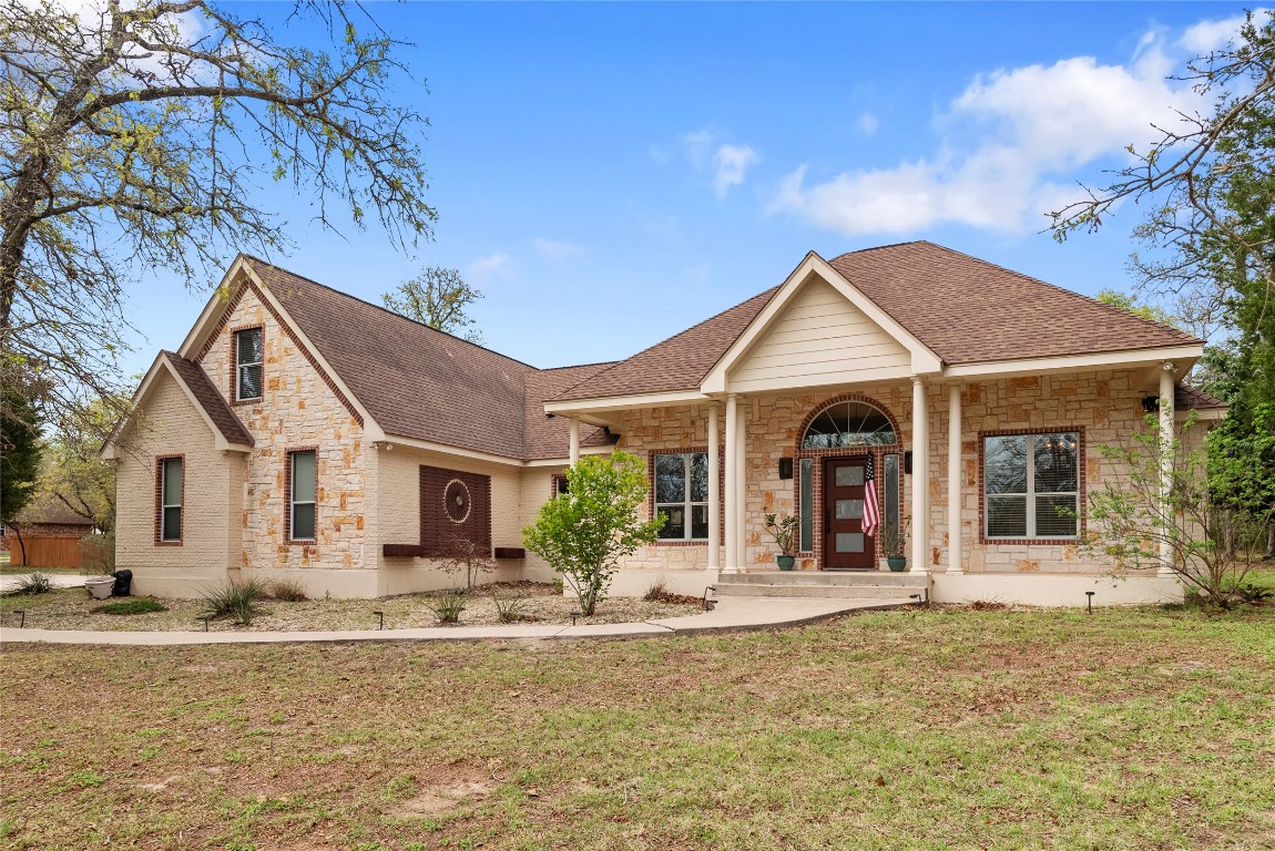 View of front of house with stone siding, a shingled roof, and a front lawn