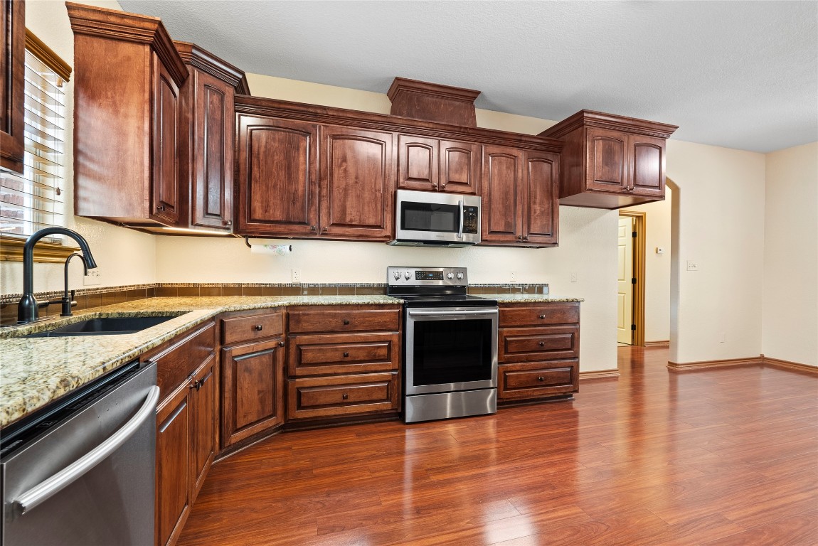 330 Arbors Circle Elgin, TX 78621 - Photo 6 of 39 Kitchen featuring dark wood-style floors, light stone countertops, a sink, and stainless steel appliances