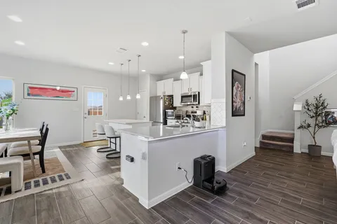 a kitchen with stainless steel appliances kitchen island granite countertop a refrigerator a stove a sink a dining table and chairs with wooden floor