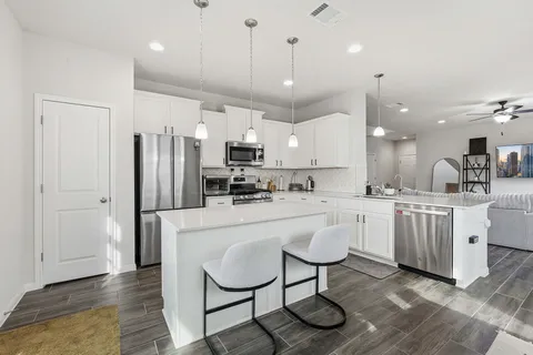 a kitchen with kitchen island granite countertop a refrigerator a sink dishwasher a oven a dining table and chairs with wooden floor