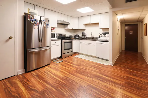 a kitchen with stainless steel appliances granite countertop a refrigerator oven a sink and white cabinets with wooden floor