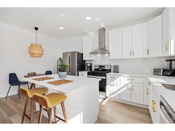 a kitchen with stainless steel appliances kitchen island granite countertop a sink dishwasher a stove a kitchen island with chairs and white cabinets