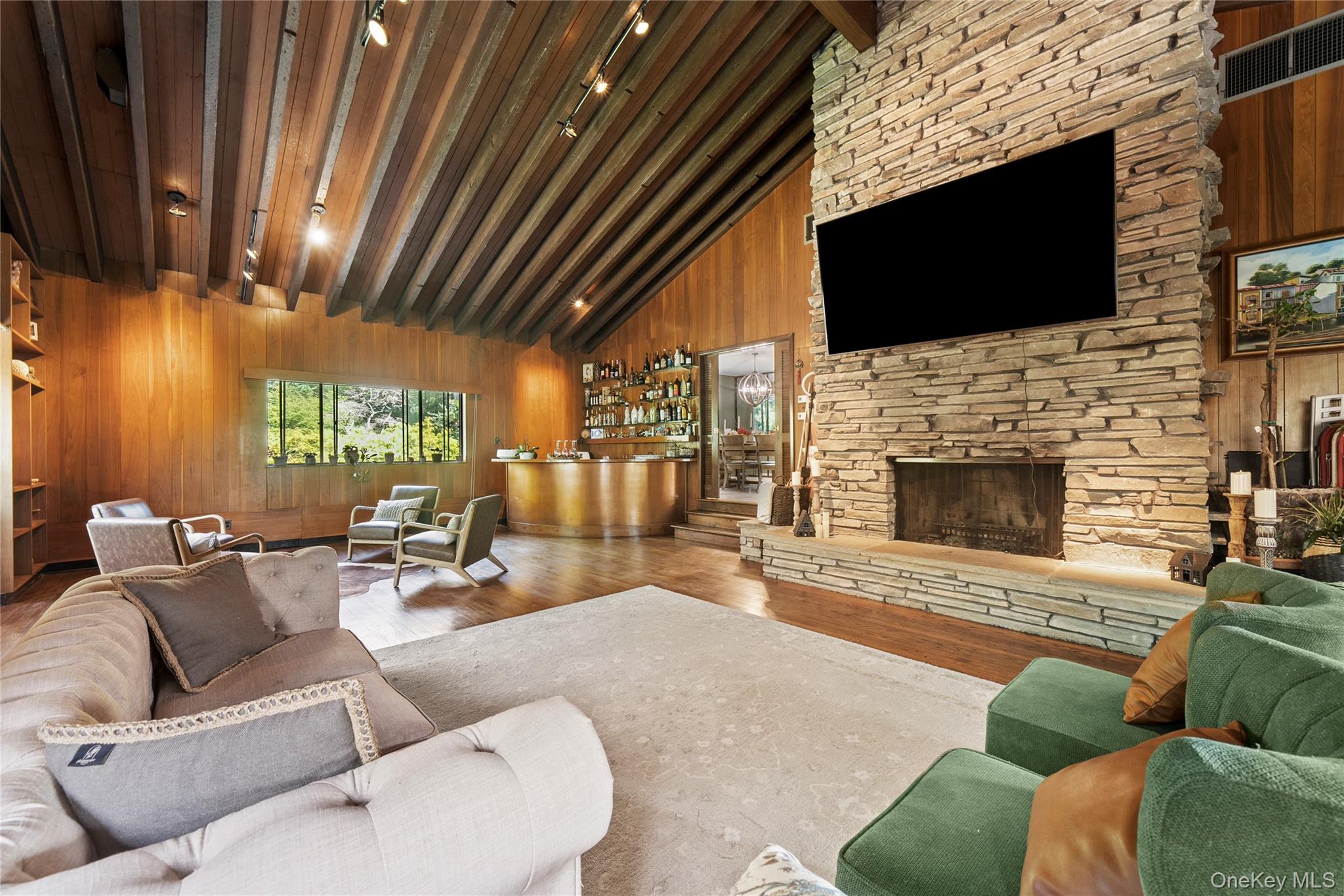 55 Rolling Hill Lane Old Westbury, NY 11568 - Photo 11 of 48 Living room with wood walls, beam ceiling, wood finished floors, a stone fireplace, and high vaulted ceiling