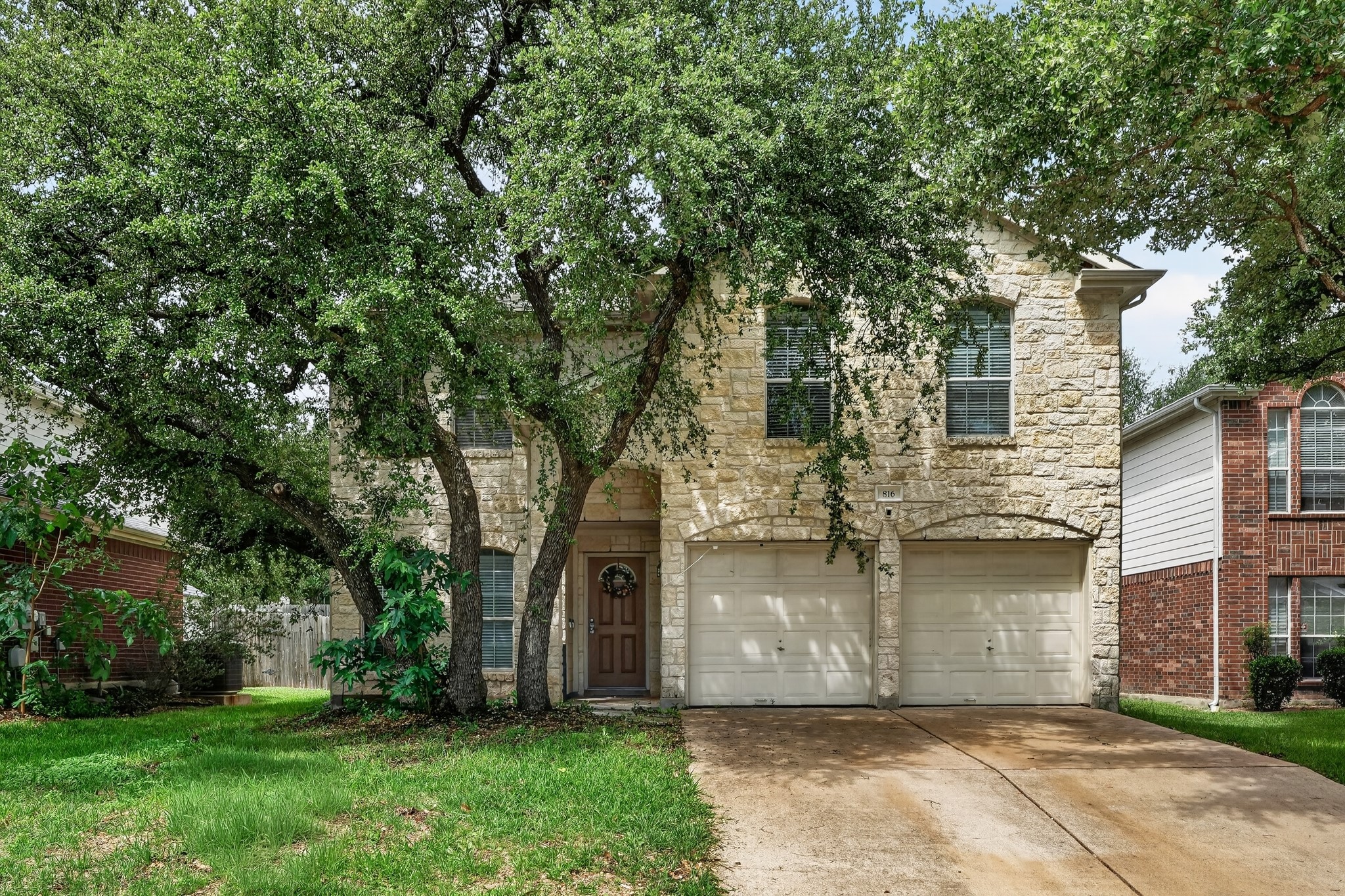 Stone facade residence featuring a two-car garage, mature trees, and a concrete driveway