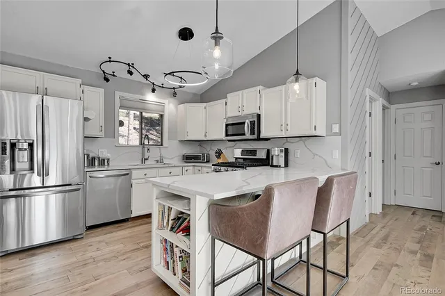 a kitchen with kitchen island granite countertop a sink a stove a refrigerator cabinets and chairs