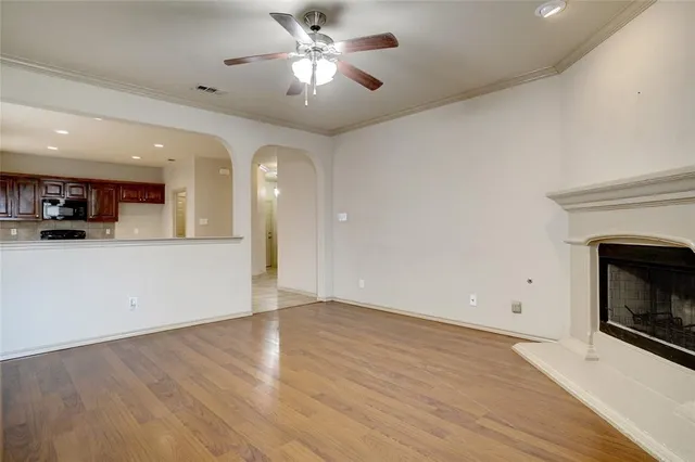an empty room with wooden floor a ceiling fan a fireplace and windows