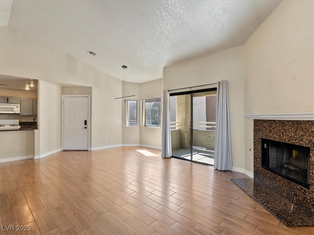 5052 South Rainbow Boulevard, Unit 201 Las Vegas, NV 89118 - Photo 5 of 24 Unfurnished living room with a premium fireplace, vaulted ceiling, light wood finished floors, and a textured ceiling