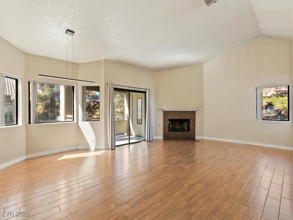 5052 South Rainbow Boulevard, Unit 201 Las Vegas, NV 89118 - Photo 6 of 24 Unfurnished living room featuring light wood-style floors, a fireplace, vaulted ceiling, and a textured ceiling
