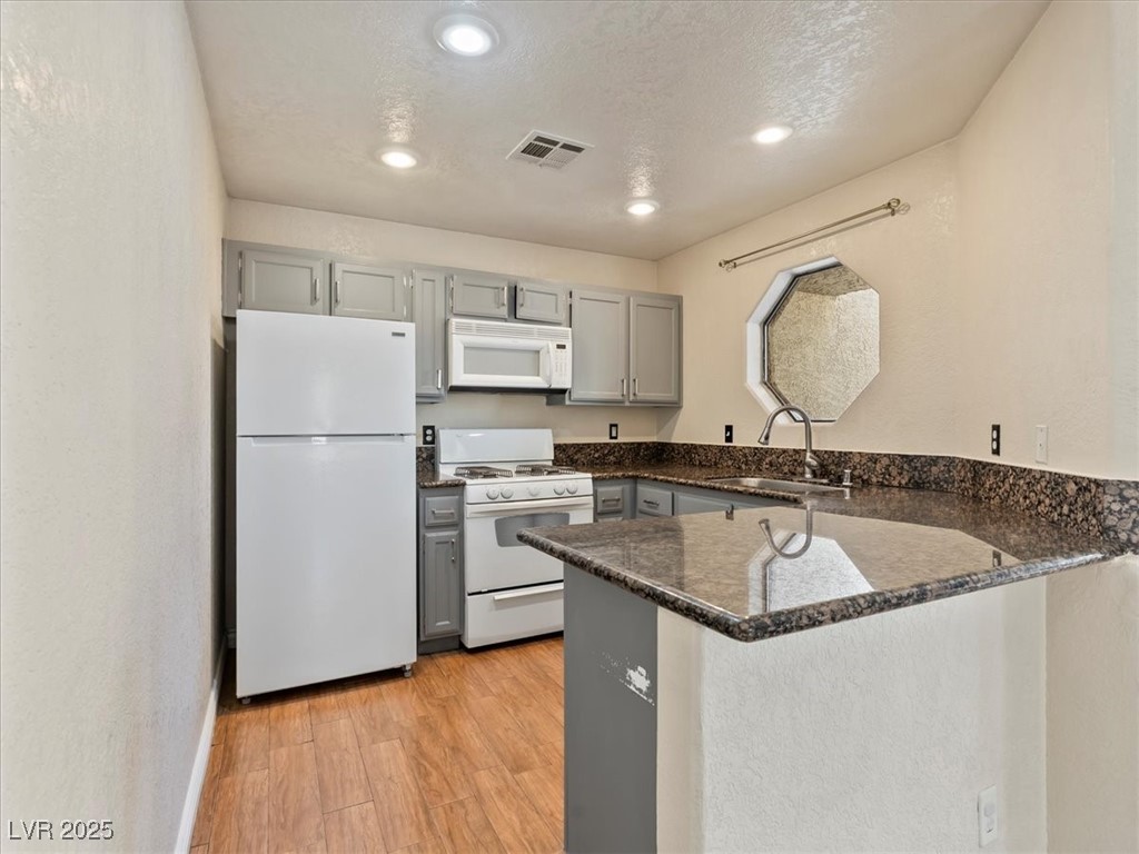 5052 South Rainbow Boulevard, Unit 201 Las Vegas, NV 89118 - Photo 9 of 24 Kitchen with gray cabinetry, white appliances, dark stone counters, light wood-style floors, and a peninsula