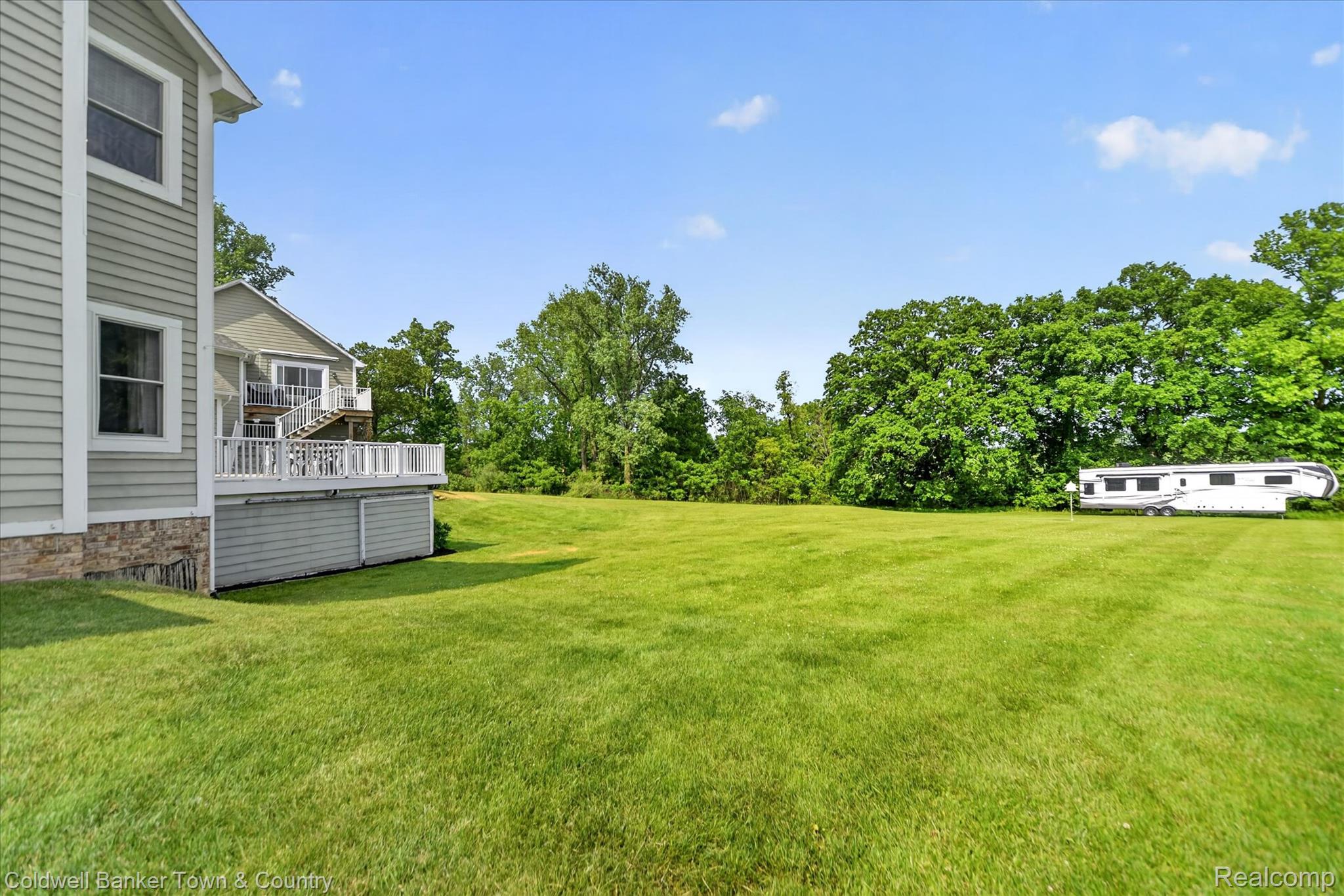 918 Gray Fox Court Howell, MI 48843 - Photo 66 of 84 Expansive green lawn bordering mature trees, featuring a multi-level rear deck with white railings and an exterior staircase