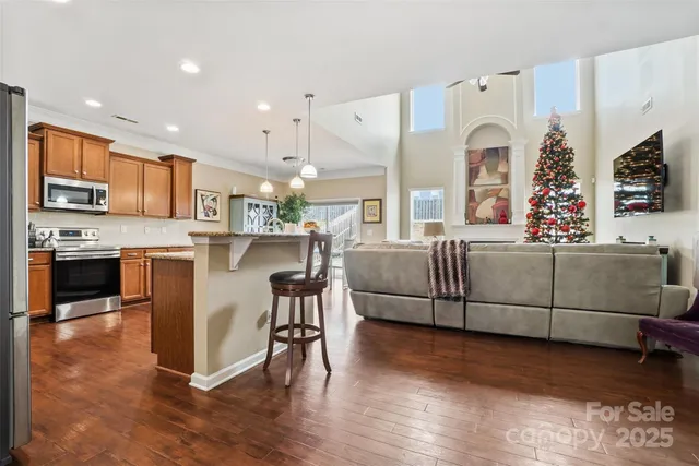 a living room with stainless steel appliances kitchen island granite countertop a stove a sink a refrigerator cabinets and a dining table with wooden floor