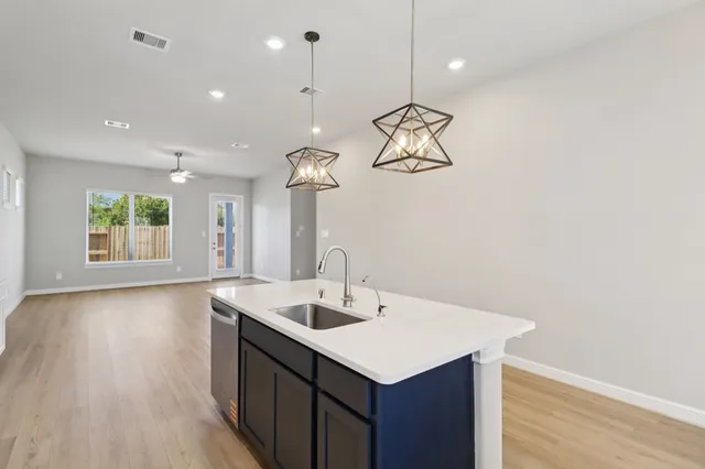 a kitchen with a sink a chandelier stainless steel appliances and wooden floor