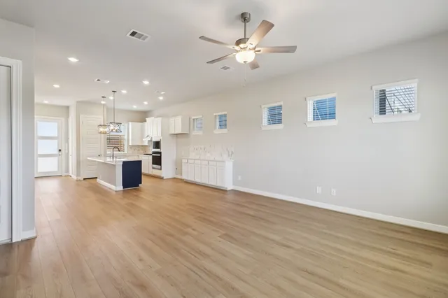 a view of an empty room with wooden floor and a kitchen