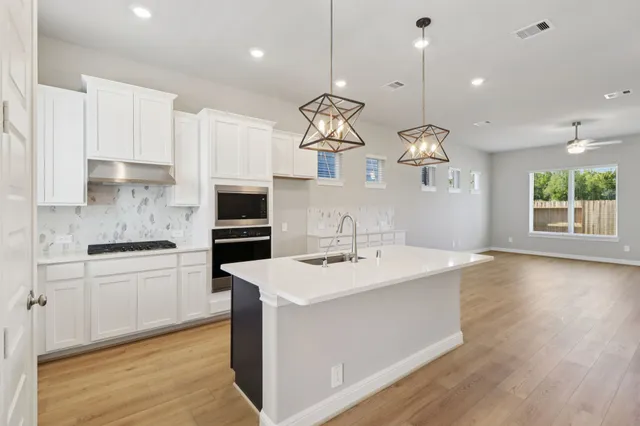 a kitchen with a sink a microwave oven a stove and white cabinets with wooden floor