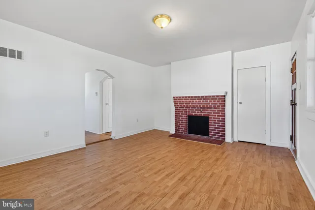 a view of an empty room with wooden floor and a fireplace