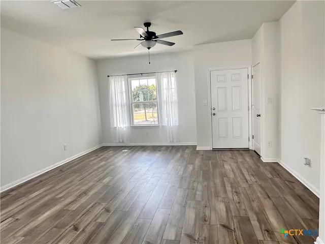 a view of an empty room with wooden floor and a window