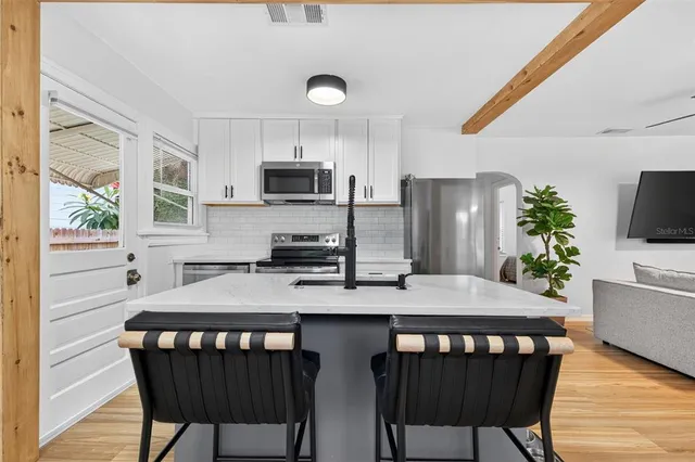 a kitchen with stainless steel appliances granite countertop a stove a refrigerator a microwave a dining table and chairs with wooden floor