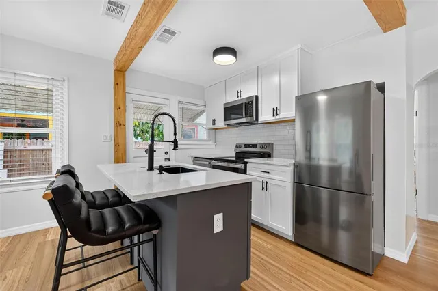 a kitchen with stainless steel appliances granite countertop a refrigerator a sink a stove a dining table and chairs with wooden floor