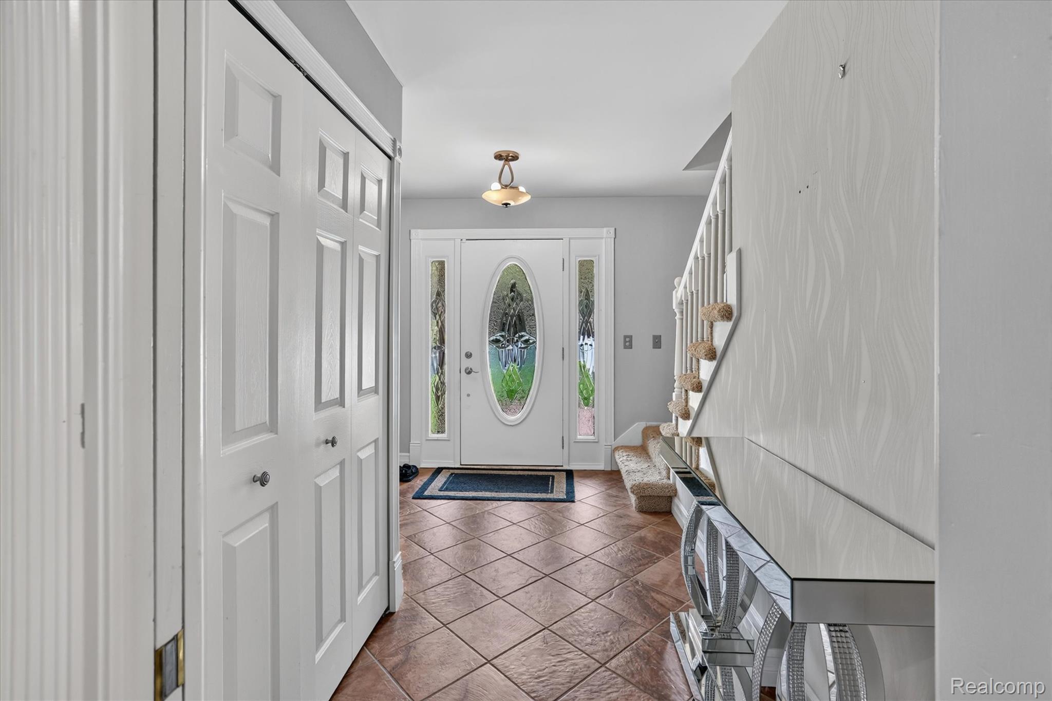 7186 East River Road Flushing, MI 48433 - Photo 4 of 47 Entryway featuring terracotta-style tile flooring, white bi-fold closet doors, a white front door with an oval-shaped leaded glass insert, and sidelights with matching leaded glass