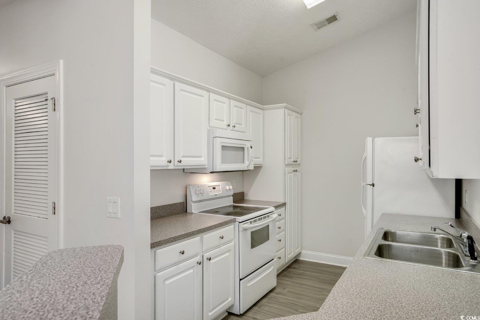 1113 Peace Pipe Place, Unit 204 Myrtle Beach, SC 29579 - Photo 5 of 27 Kitchen with white appliances, white cabinets, light wood-type flooring, light countertops, and a textured ceiling