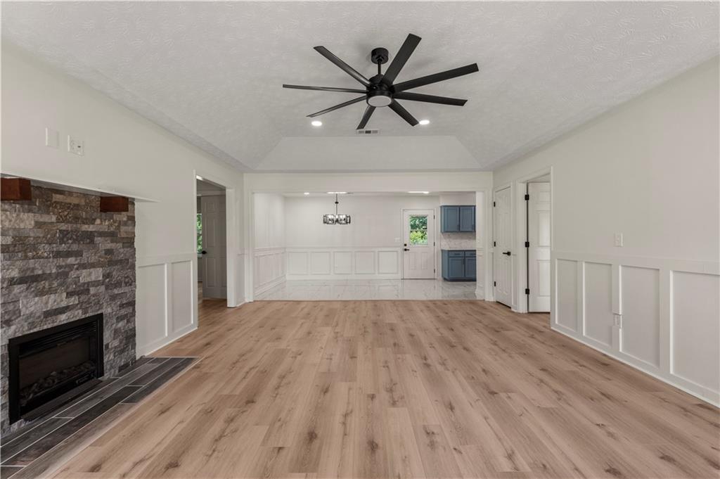 766 Lee Road Phenix City, AL 36870 - Photo 3 of 30 Unfurnished living room featuring light wood-type flooring, ceiling fan, a decorative wall, a stone fireplace, and a chandelier