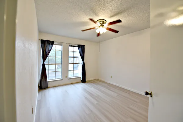 an empty room with wooden floor fan and windows