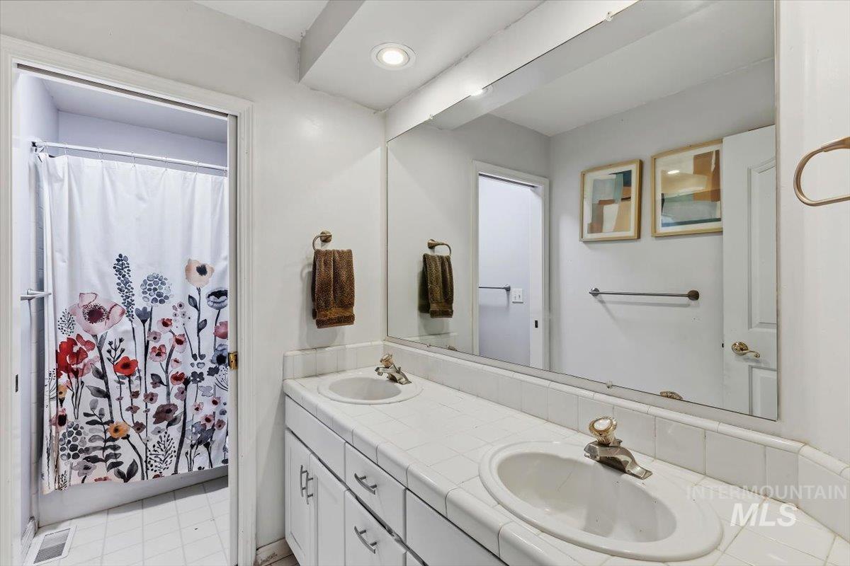 8001 West Innsbrook Court Boise, ID 83704 - Photo 26 of 39 Dual sink vanity with white tiled countertop and integrated sinks, a large wall-mounted mirror, recessed lighting, and white cabinetry