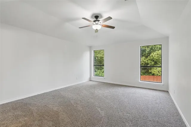 an empty room with chandelier fan and windows