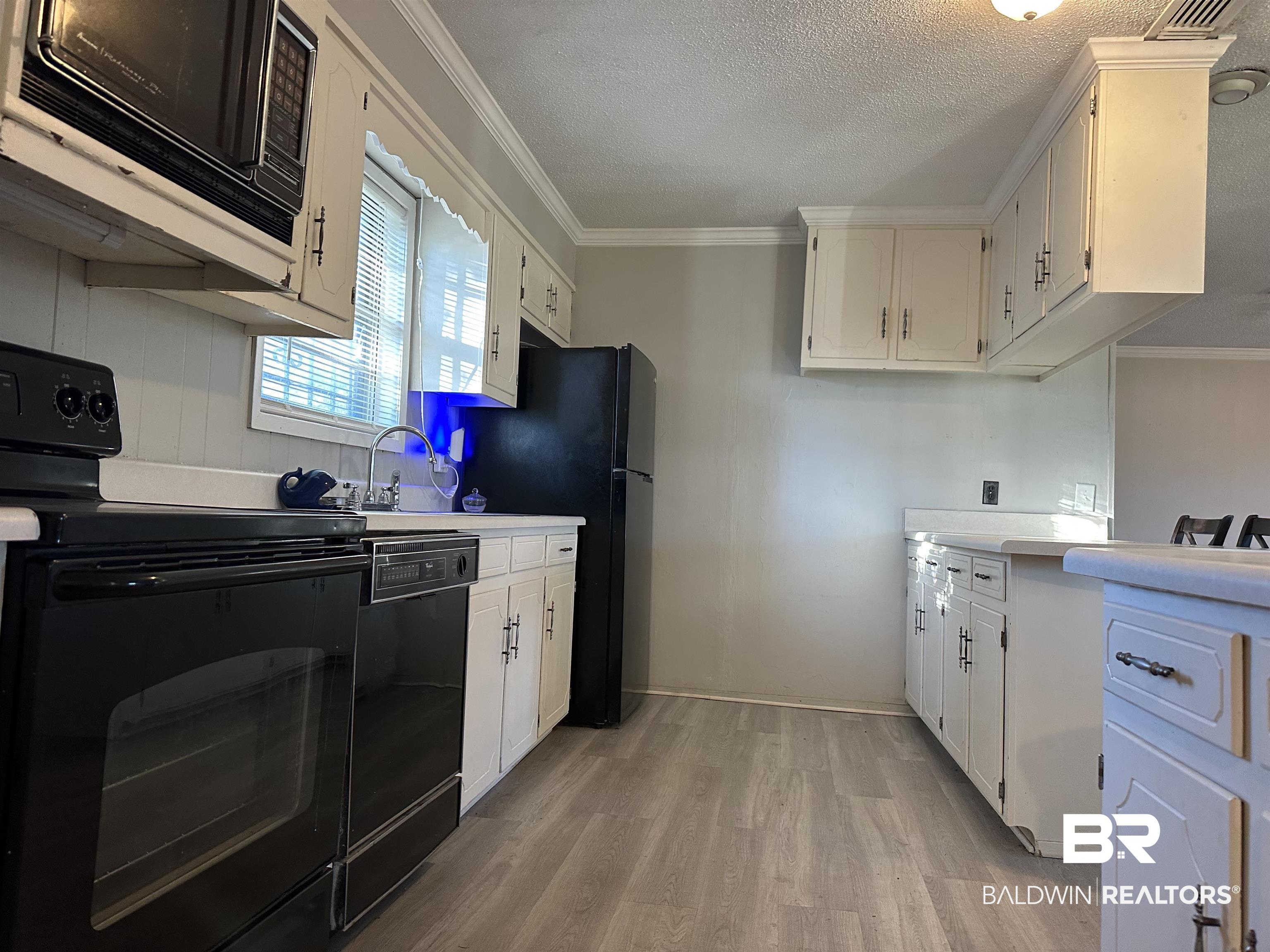 3451 Kirkland Road Brewton, AL 36426 - Photo 6 of 17 Kitchen with crown molding, light hardwood / wood-style flooring, white cabinets, and black appliances