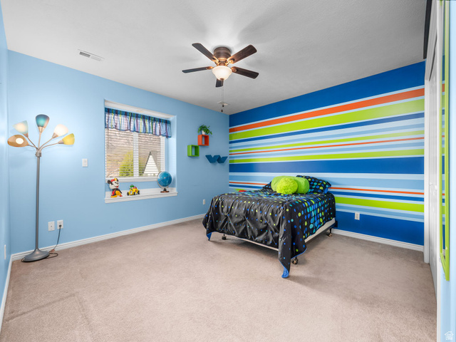 6849 North Black Powder Road Mountain Green, UT 84050 - Photo 19 of 43 Carpeted room featuring a window with blinds, ceiling fan with integrated lighting, a colorful accent wall, and built-in shelving