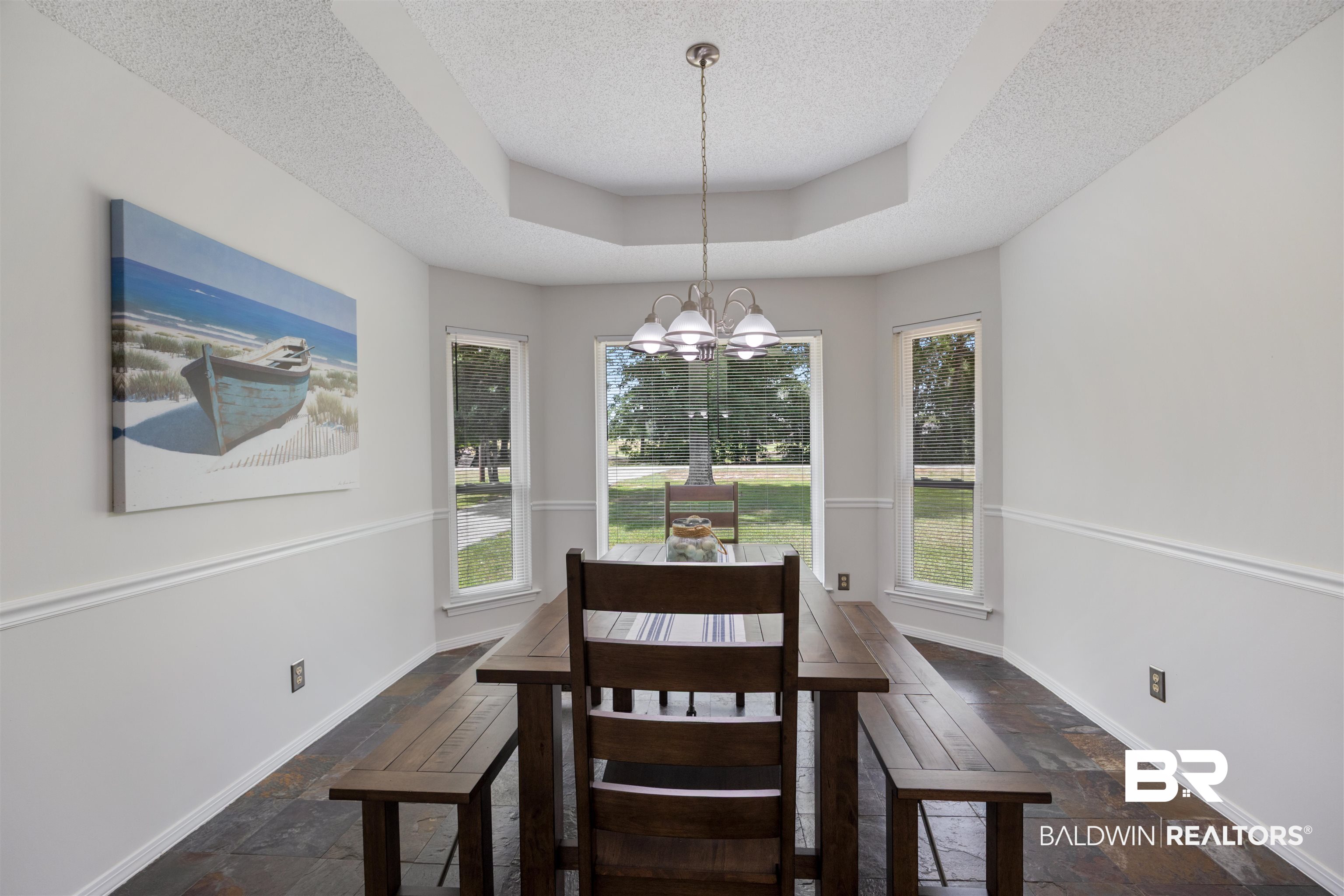 9771 Clarke Ridge Road Foley, AL 36535 - Photo 34 of 72 Dining area with a tray ceiling, a textured ceiling, stone tile flooring, baseboards, and a chandelier.