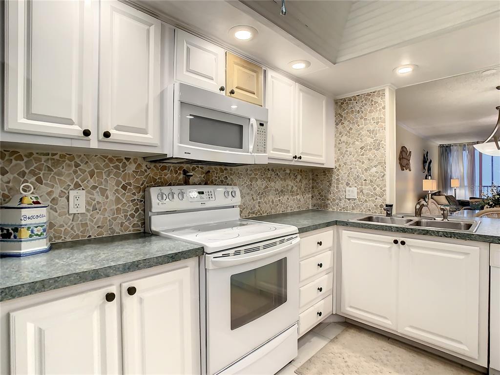 18304 Gulf Boulevard, Unit 116 Redington Shores, FL 33708 - Photo 13 of 51 a kitchen with granite countertop white cabinets and white appliances