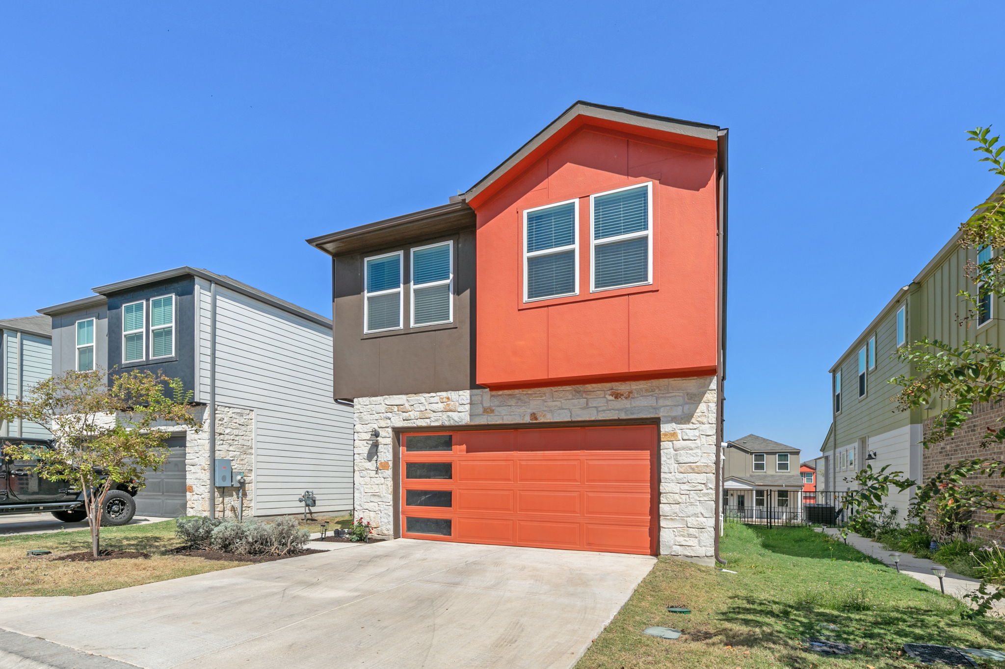 7312 Travertine Spring Drive Austin, TX 78744 - Photo 2 of 32 Modern facade with a vibrant orange garage door and stone accents creates inviting curb appeal.