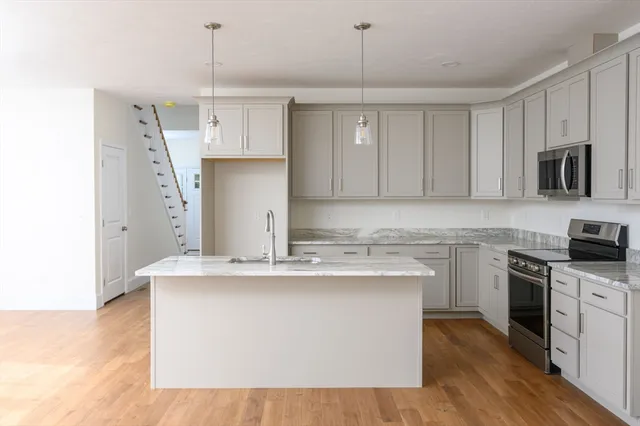 a kitchen with stainless steel appliances granite countertop a sink a stove a refrigerator and island with wooden floor