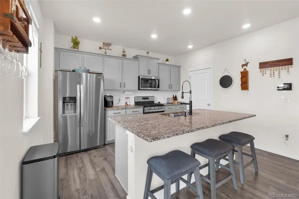 a kitchen with stainless steel appliances granite countertop a stove a sink a microwave a refrigerator white cabinets and wooden floor