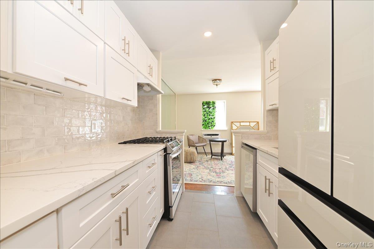 320 East Shore Road, Unit 4C Great Neck, NY 11023 - Photo 13 of 29 Kitchen with appliances with stainless steel finishes, white cabinets, light stone countertops, recessed lighting, and decorative backsplash